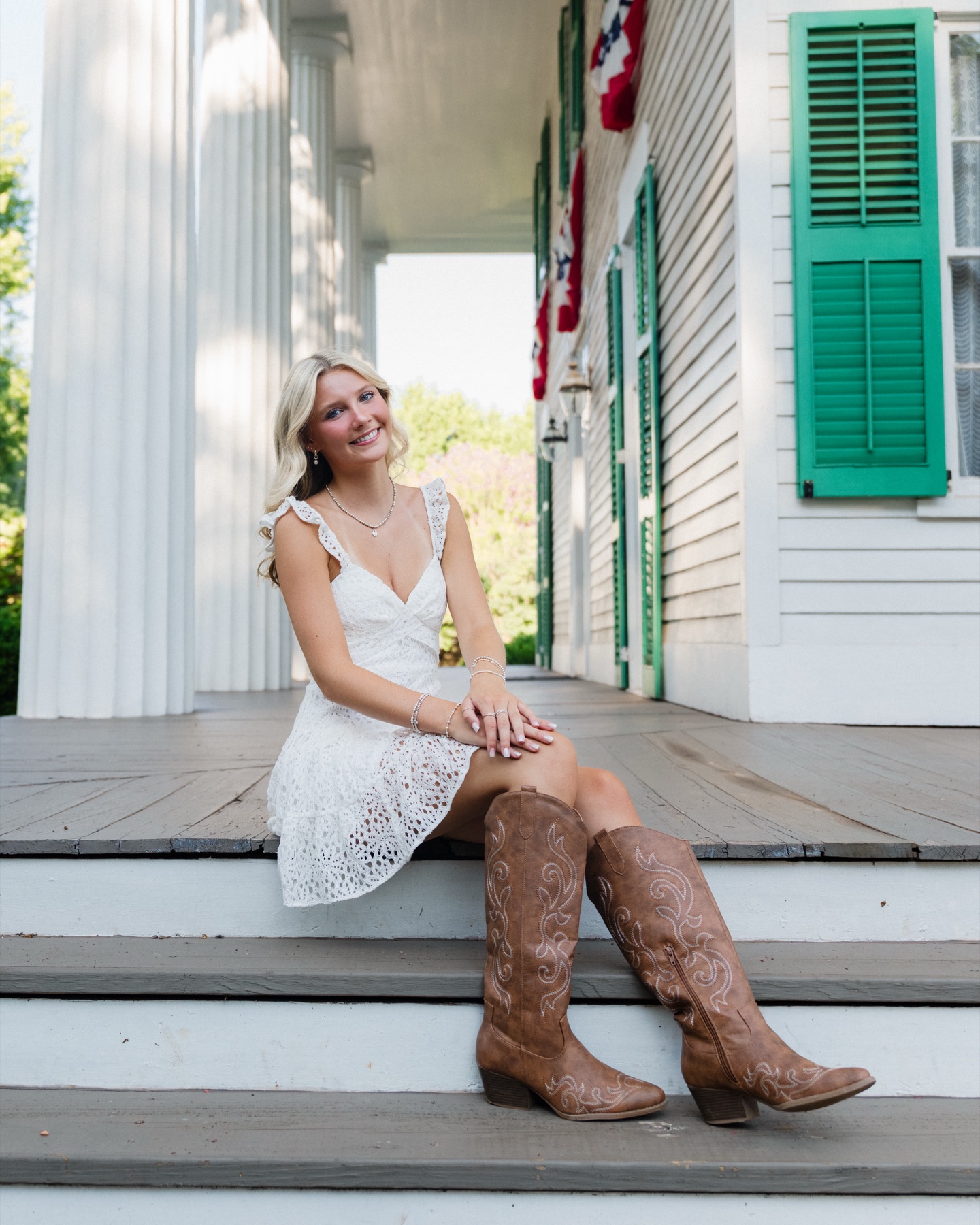 Senior portrait in a white dress and boots beside green shutters