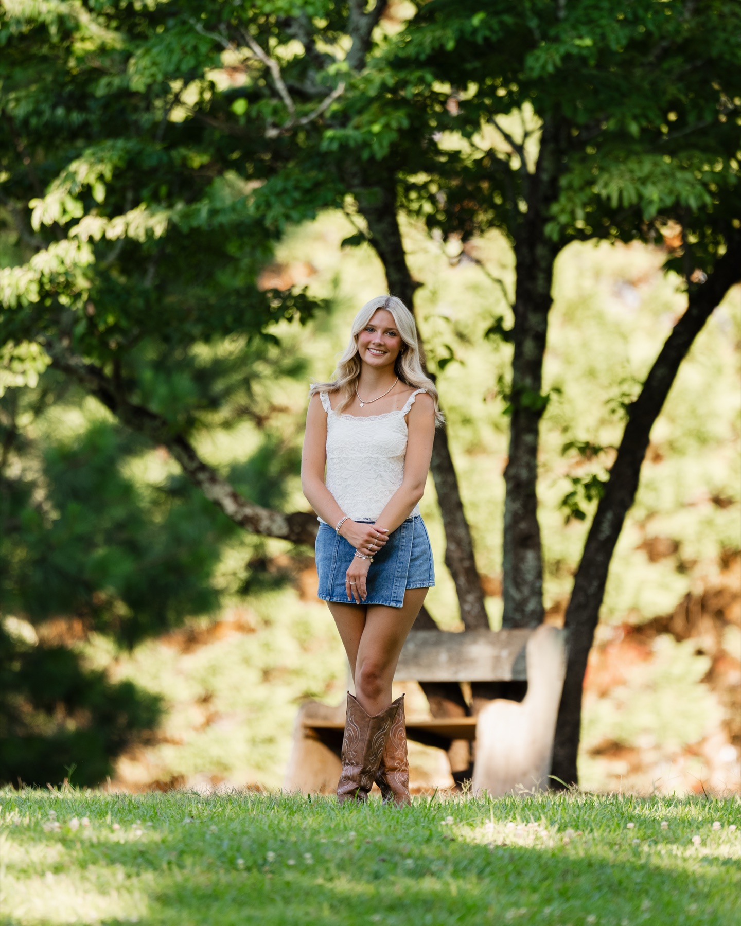 Senior portrait beneath leafy trees, wearing a white top and denim skirt