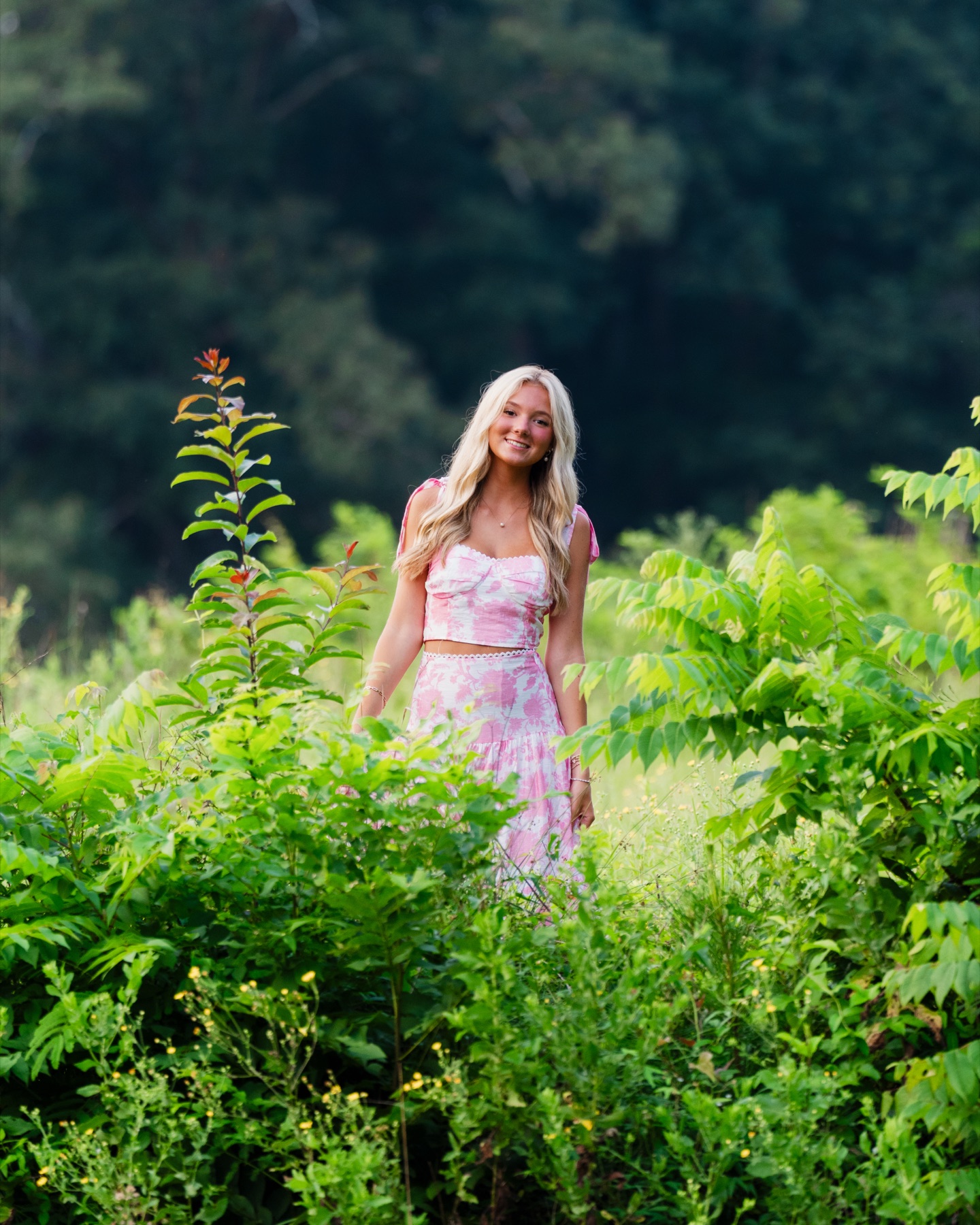 Senior portrait in a pink dress surrounded by greenery